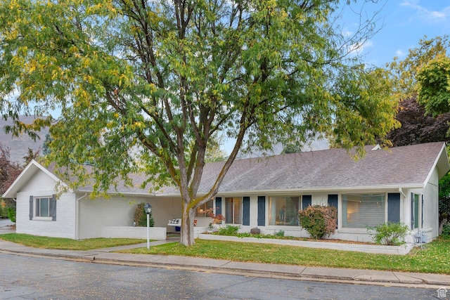 ranch-style house with a front lawn, brick siding, and roof with shingles