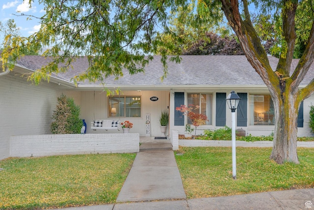 ranch-style home with covered porch, a shingled roof, and a front lawn