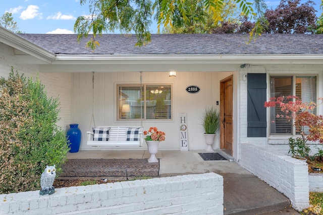 entrance to property featuring roof with shingles, a porch, and brick siding