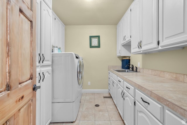 laundry area featuring light tile patterned floors, baseboards, washing machine and clothes dryer, cabinet space, and a sink