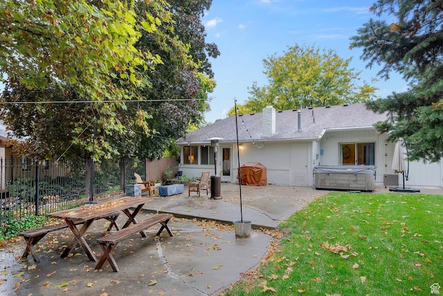 rear view of house with a patio, fence, a yard, a chimney, and a hot tub