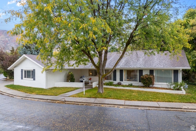 single story home featuring brick siding, a front yard, and roof with shingles