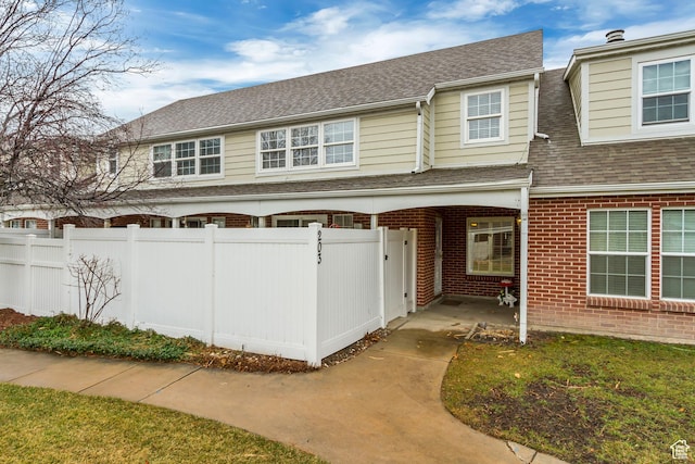 view of front of property with brick siding, a shingled roof, and fence