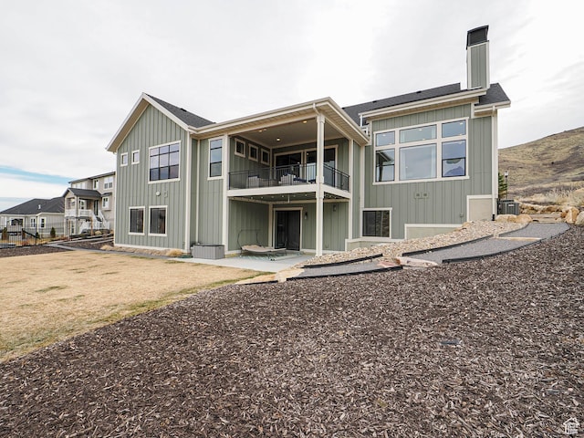 back of property featuring a balcony, board and batten siding, a chimney, and a patio area