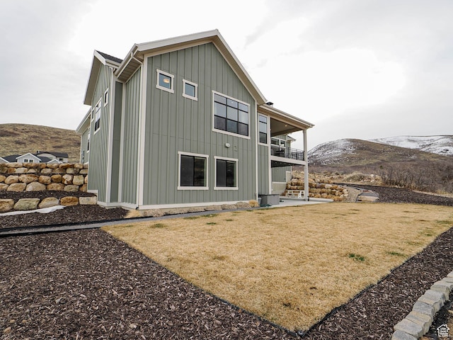 back of house with a yard, a mountain view, board and batten siding, a balcony, and a patio area