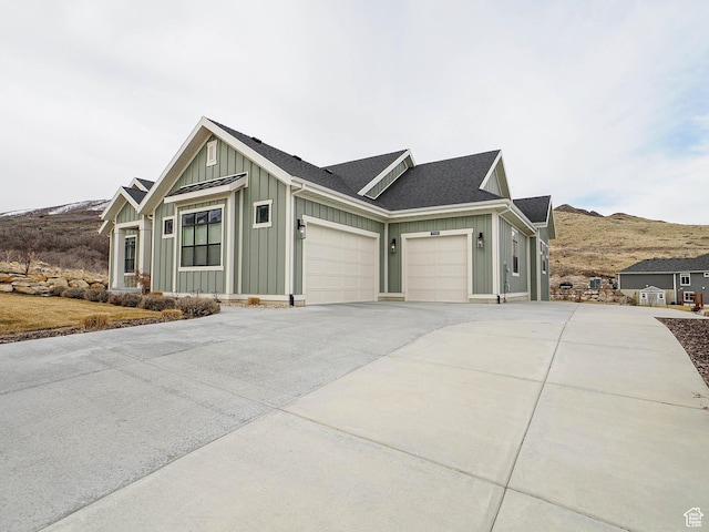 view of property exterior with driveway, a mountain view, board and batten siding, an attached garage, and a shingled roof