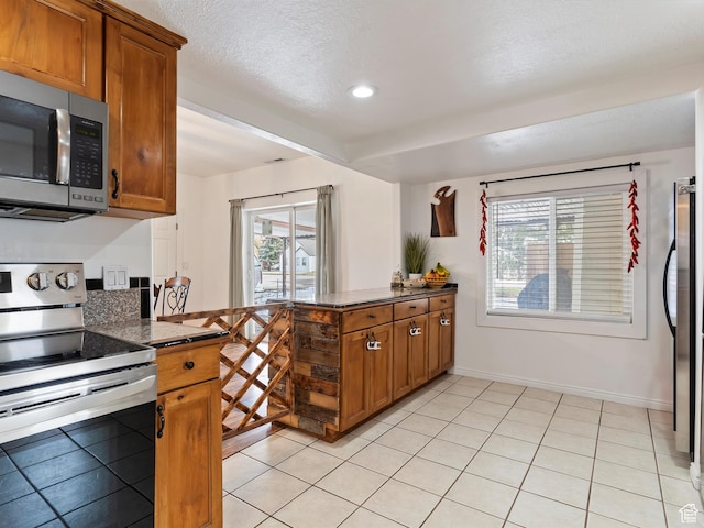 3911 W 2250 N, Corinne, UT 84307 - kitchen with a healthy amount of sunlight, a peninsula, light tile patterned flooring, stainless steel appliances, and brown cabinets