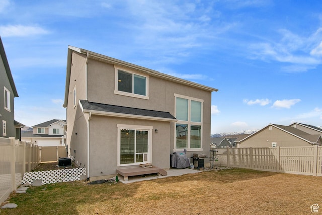 rear view of property featuring a yard, stucco siding, central AC, and a fenced backyard