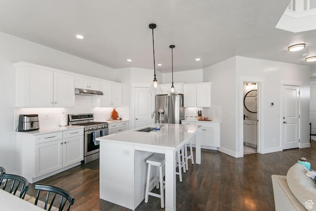 kitchen with a sink, under cabinet range hood, a kitchen breakfast bar, stainless steel appliances, and dark wood-style flooring