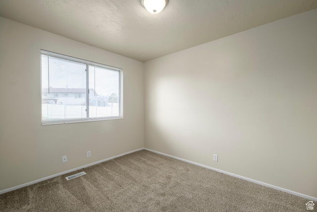 carpeted spare room featuring visible vents, baseboards, and a textured ceiling