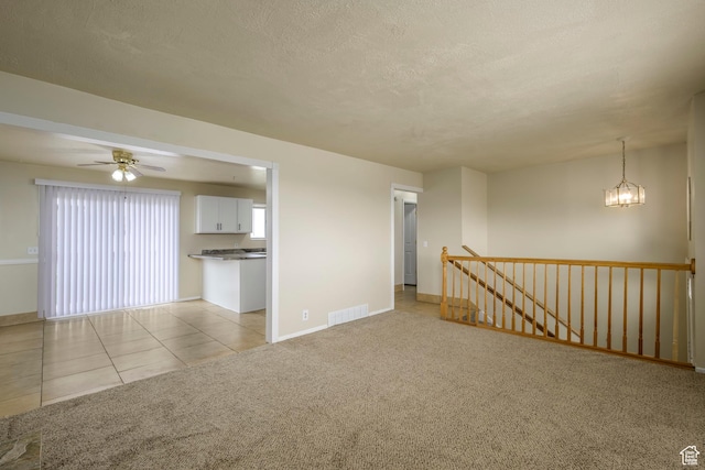 spare room featuring visible vents, light tile patterned flooring, a textured ceiling, light carpet, and ceiling fan with notable chandelier