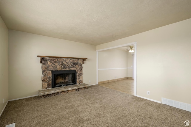 unfurnished living room with carpet, visible vents, a ceiling fan, a stone fireplace, and a textured ceiling