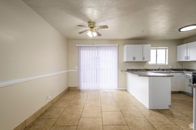 kitchen with light tile patterned floors, a ceiling fan, baseboards, a peninsula, and white cabinets