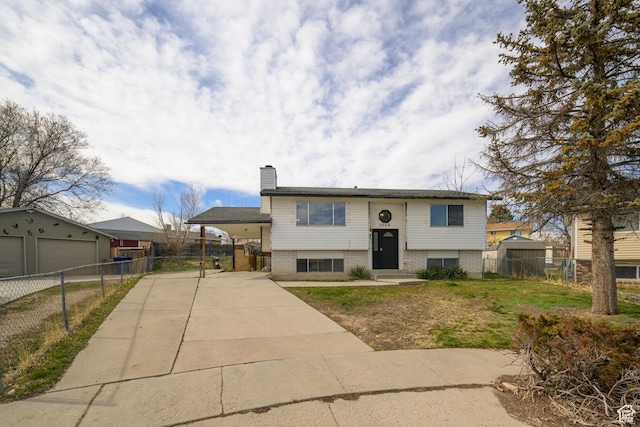 split foyer home featuring fence, a chimney, concrete driveway, a carport, and brick siding