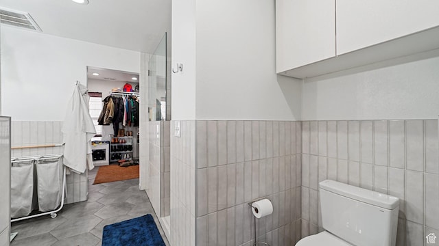 bathroom with visible vents, toilet, wainscoting, tile patterned floors, and tile walls