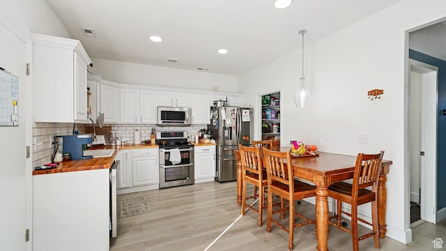 kitchen with wooden counters, backsplash, appliances with stainless steel finishes, and light wood-style floors