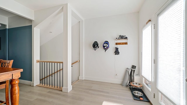 corridor with an upstairs landing, light wood-style floors, and baseboards