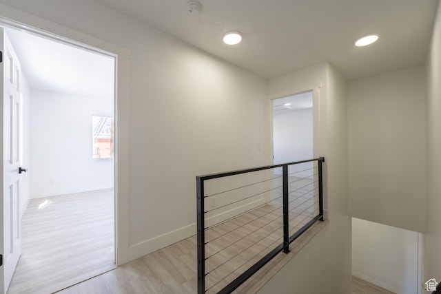 corridor with recessed lighting, light wood-type flooring, an upstairs landing, and baseboards