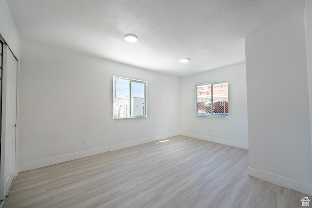 unfurnished room with light wood-style floors, baseboards, and a textured ceiling