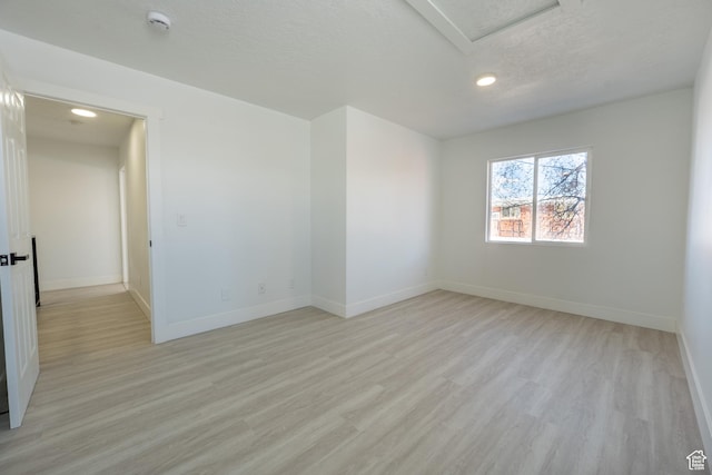 unfurnished room with light wood-type flooring, baseboards, a textured ceiling, and attic access