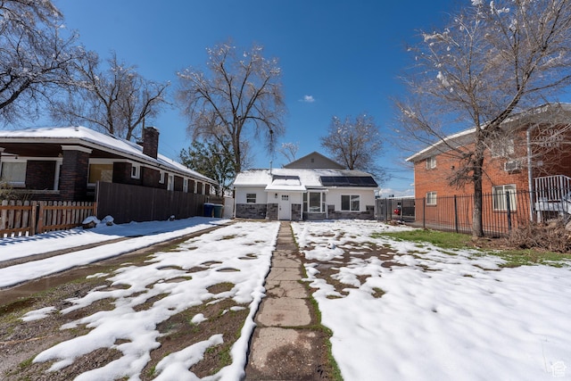 snow covered house with brick siding, a chimney, and fence