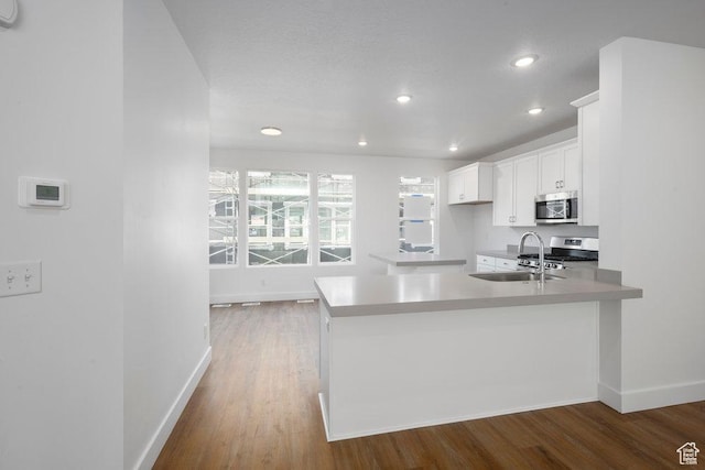 kitchen featuring baseboards, appliances with stainless steel finishes, wood finished floors, white cabinets, and a sink