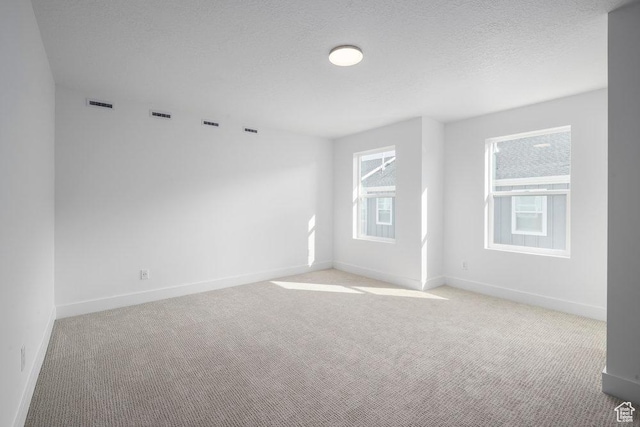 spare room with visible vents, baseboards, light colored carpet, and a textured ceiling