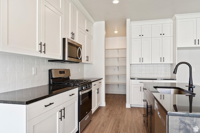 kitchen featuring a sink, white cabinetry, appliances with stainless steel finishes, light wood-style flooring, and dark stone countertops