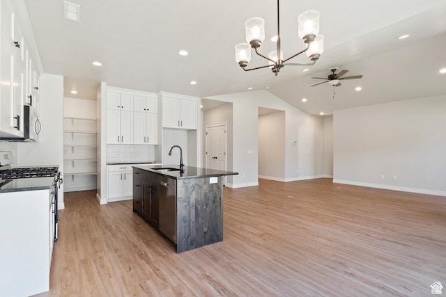 kitchen with stainless steel appliances, ceiling fan with notable chandelier, a sink, dark countertops, and light wood-style floors