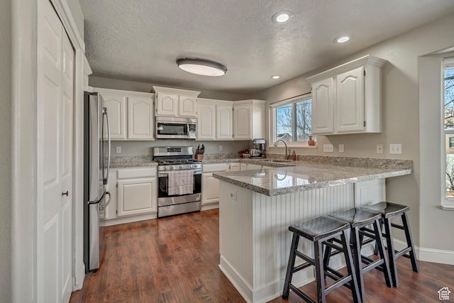 kitchen with a peninsula, a kitchen breakfast bar, white cabinets, stainless steel appliances, and a sink