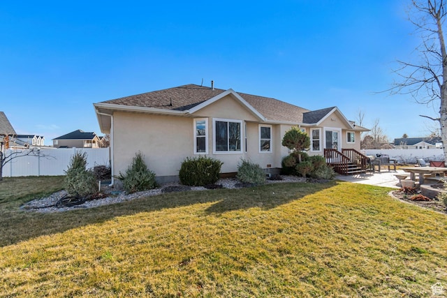 back of property with fence, roof with shingles, stucco siding, a patio area, and a lawn