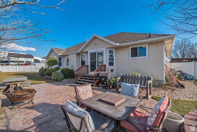 back of property with a fire pit, fence, roof with shingles, stucco siding, and a patio area