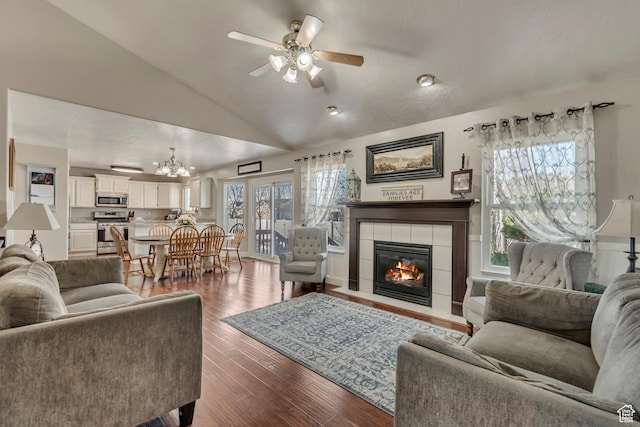 living area with lofted ceiling, dark wood finished floors, a fireplace, and ceiling fan with notable chandelier