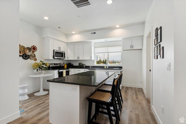 971 W 1700 S Unit 114, Salt Lake City, UT 84104 - kitchen with light wood finished floors, visible vents, dark countertops, white cabinets, and stainless steel appliances