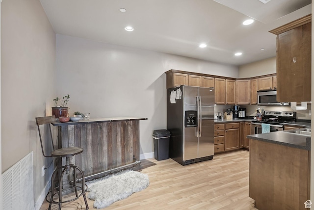 kitchen with recessed lighting, stainless steel appliances, dark countertops, visible vents, and light wood-style flooring