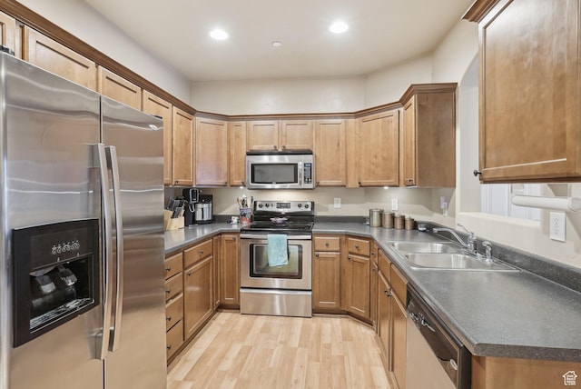 kitchen with dark countertops, a sink, stainless steel appliances, light wood-style flooring, and recessed lighting