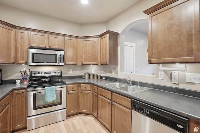 kitchen featuring dark countertops, a sink, arched walkways, light wood-style flooring, and appliances with stainless steel finishes