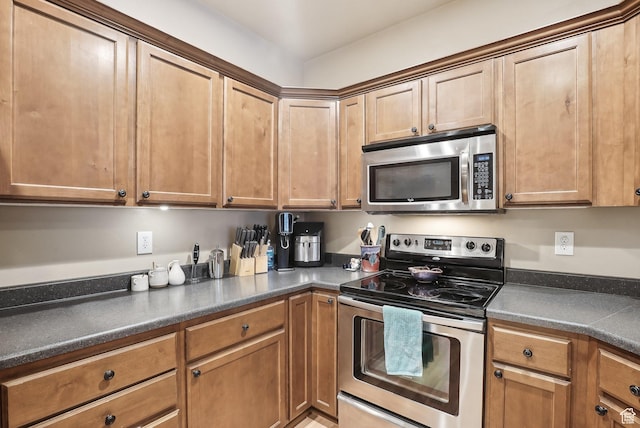 kitchen featuring brown cabinets, dark countertops, and appliances with stainless steel finishes