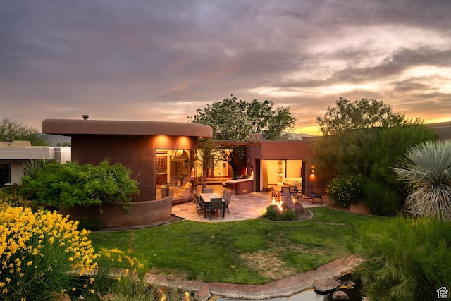 2336 W Entrada Trl Unit 44, St George, UT 84770 - back of house at dusk with a patio area, a lawn, and stucco siding