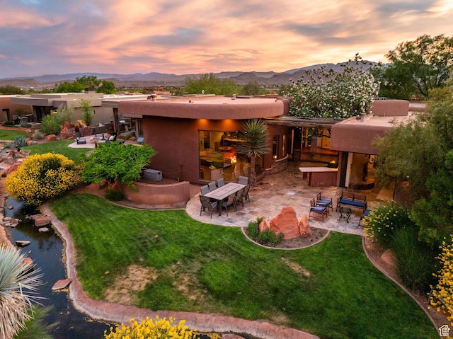 2336 W Entrada Trl Unit 44, St George, UT 84770 - back of house at dusk featuring a patio, a mountain view, stucco siding, and a lawn
