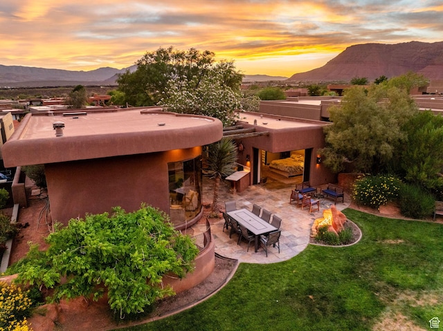 2336 W Entrada Trl Unit 44, St George, UT 84770 - back of property at dusk featuring a mountain view, a patio, a lawn, stucco siding, and an outdoor fire pit