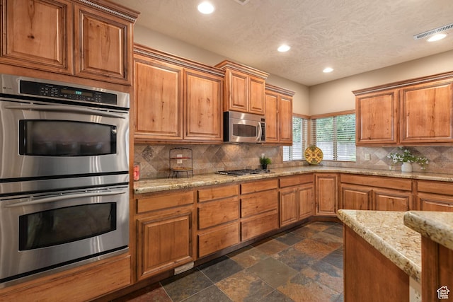 1815 N Red Mountain Dr, Santa Clara, UT 84765 - kitchen with stone tile floors, visible vents, appliances with stainless steel finishes, brown cabinets, and backsplash