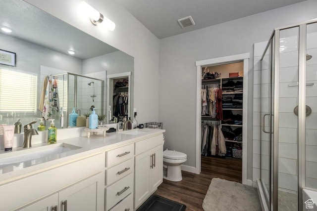 4268 S Steele Creek Ct E, Millcreek, UT 84107 - bathroom featuring a walk in closet, double vanity, a shower stall, toilet, and wood finished floors