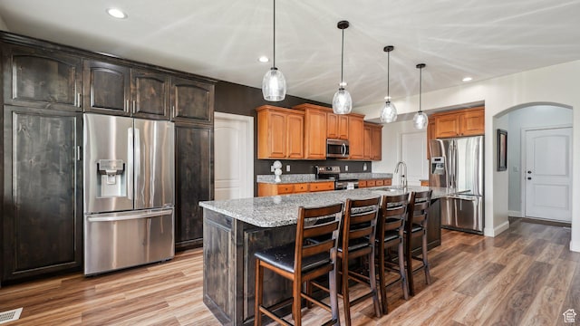 125 N 1430 E, Spanish Fork, UT 84660 - kitchen with appliances with stainless steel finishes, arched walkways, a sink, light stone counters, and a kitchen island with sink