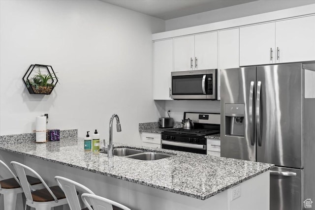 kitchen featuring a sink, a kitchen breakfast bar, stainless steel appliances, a peninsula, and white cabinets