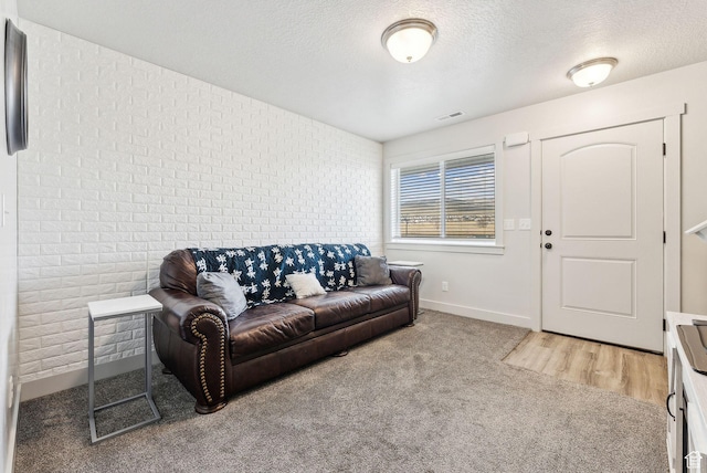 carpeted living area with visible vents, brick wall, a textured ceiling, and baseboards