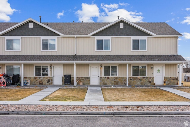 multi unit property featuring a front lawn, covered porch, stone siding, and roof with shingles