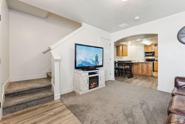 living room featuring light wood-style flooring, arched walkways, a lit fireplace, stairs, and a textured ceiling