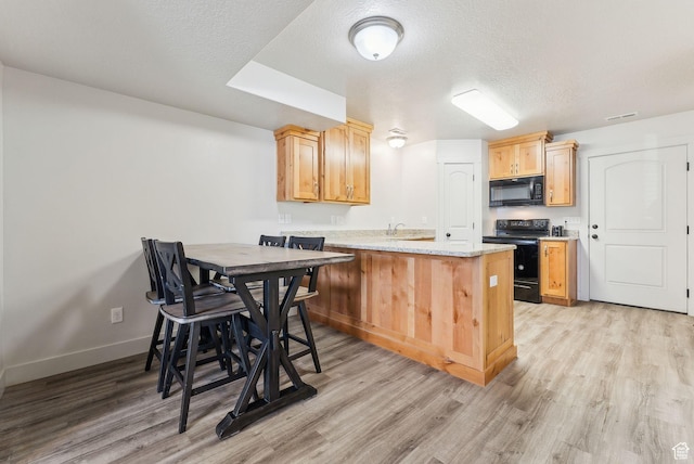 kitchen with a peninsula, light brown cabinetry, black appliances, a textured ceiling, and light wood-type flooring
