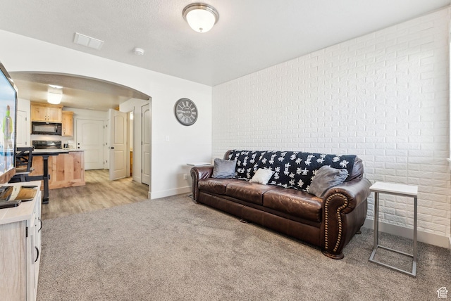 living area with visible vents, brick wall, baseboards, light colored carpet, and arched walkways